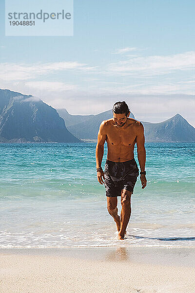 Lächelnder Mann  der am Strand aus dem blauen Wasser läuft