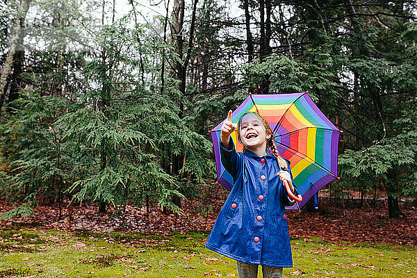 Junges Mädchen hält Regenschirm in einem Wald  zeigt und lächelt