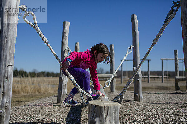 Ein kleines Mädchen klettert in einem Outdoor-Hindernisparcours auf einen Schwebebalken