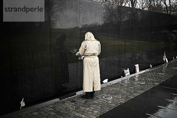 Eine Frau in einem Regenmantel blickt auf die gravierte Wand des Vietnam War Memorial.