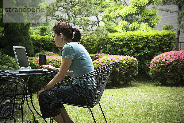 Eine Frau sitzt draußen vor einem Laptop.