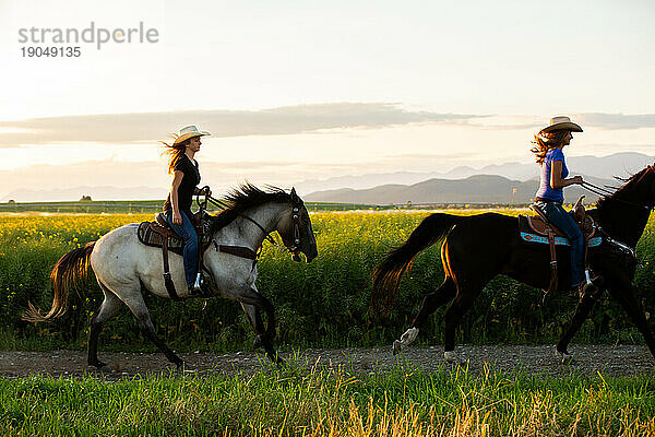 Zwei Cowgirls reiten bei Sonnenuntergang durch ein Rapsfeld