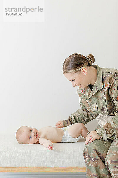 Eine Mutter im aktiven Militärdienst spielt mit ihrem Baby  während sie ihm die Windel wechselt