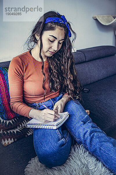 Konzentrierte Frau mit gemischter Rasse beim Schreiben in Notizbuch im Innenbereich