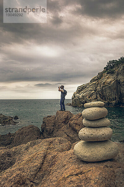 Abenteuerlustiger Mann mit Fotokamera und Fernglas erkundet einen Felsen