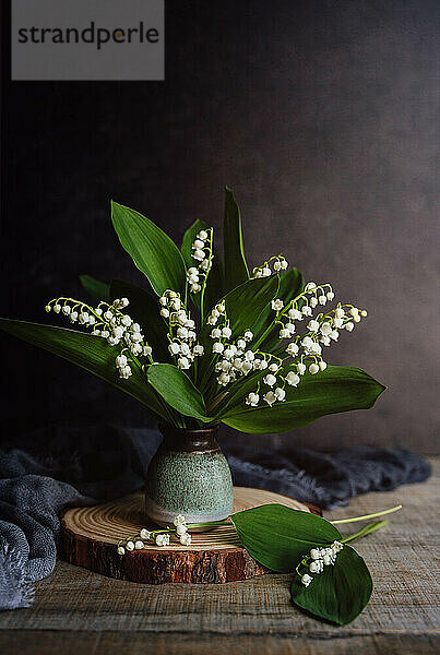 Stillleben mit einer kleinen Vase mit Maiglöckchenblüten auf einem Holztisch.