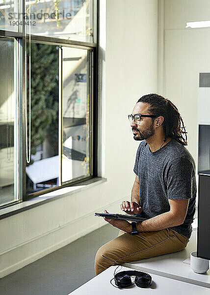 Seitenansicht eines nachdenklichen Geschäftsmannes mit Tablet-Computer  der auf dem Schreibtisch im Büro sitzt