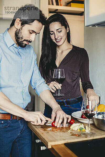 Junger Mann bereitet in der Küche das Mittagessen für seine Freundin zu  während sie ein Glas Wein trinkt