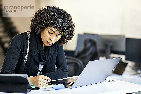 Selbstbewusste Geschäftsfrau mit lockigem Haar schreibt im Büro auf Klebezettel