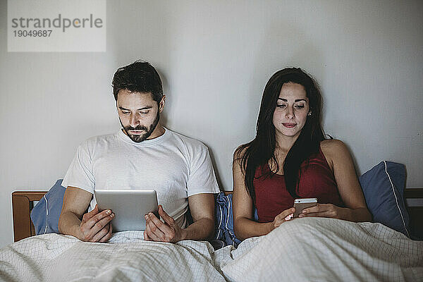 Junges Paar im Bett mit Smartphone und Tablet