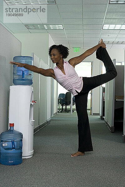 Eine leitende Frau macht Yoga am Wasserkühler  während sie bei der Arbeit in Santa Clara  Kalifornien  arbeitet.
