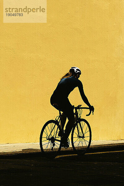 Minimalistische Silhouette einer Radfahrerin vor einer schlichten gelben Wand