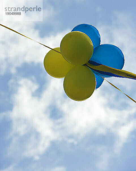 Blaue und gelbe Luftballons vor einem bewölkten blauen Himmel.