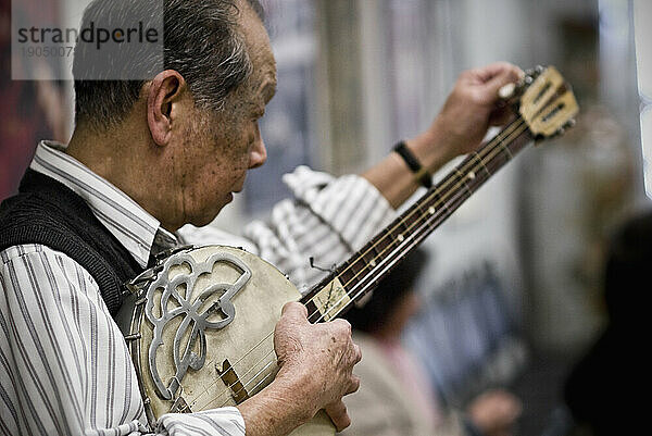 Ein älterer Mann stimmt sein Instrument  bevor er traditionelle chinesische Musik aufführt.