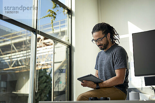 Low-Angle-Ansicht eines Geschäftsmannes mit Dreadlocks  der einen Tablet-Computer benutzt  während er im Büro sitzt