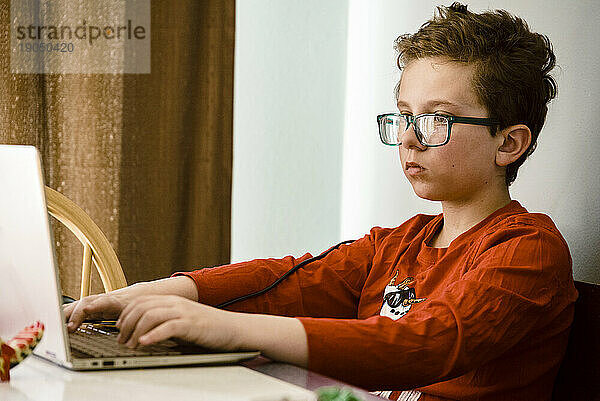 Junge konzentriert sich mit einem Laptop am Tisch.