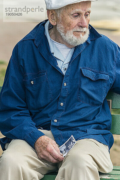 Ein älterer Mann sitzt traurig allein auf einer Parkbank.