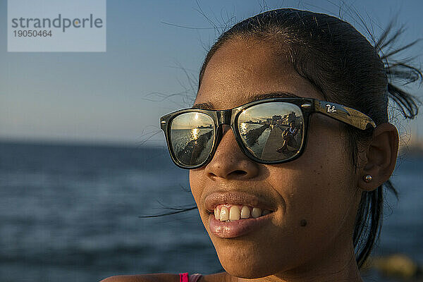 Nahaufnahme eines lächelnden kubanischen Mädchens mit verspiegelter Sonnenbrille auf dem Malecón (Avenida de Maceo)  Havanna  La Habana  Kuba.