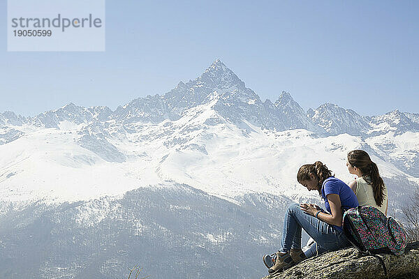 Zwei Teenager-Mädchen entspannen sich auf Felsen unterhalb des Berges