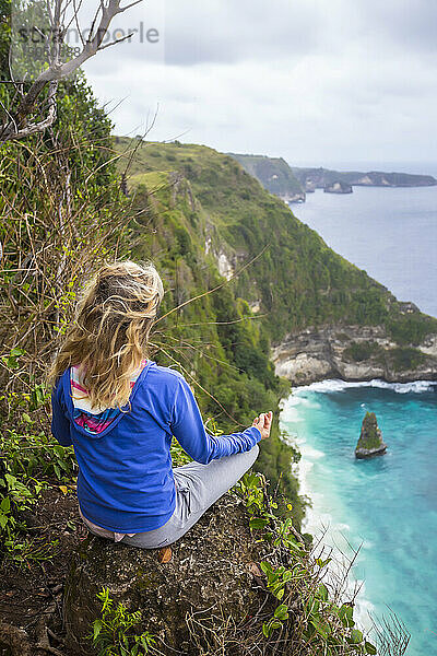 Blonde Frau meditiert am Rand einer Klippe an der Küste  Bali  Indonesien