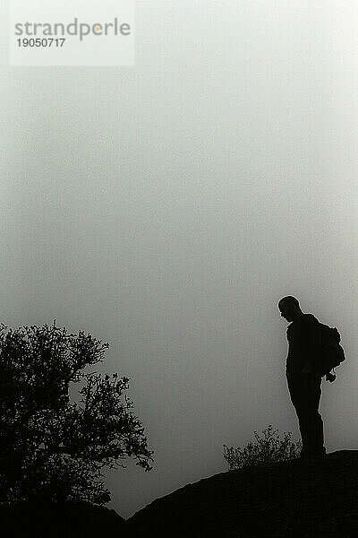 Silhouette eines Mannes  der mit einem Rucksack im Nebel steht