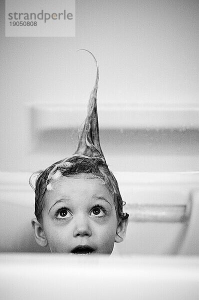 Mädchen (3-4 Jahre) nimmt ein Bad und blickt zu stacheligen Haaren auf.