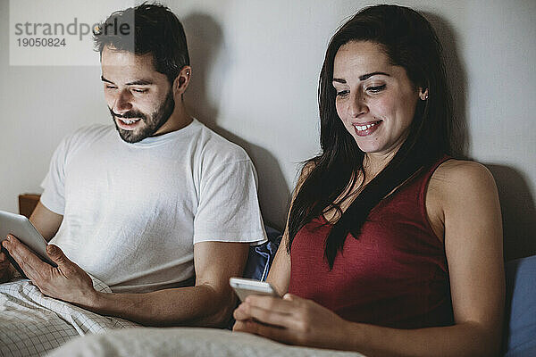 Junges Paar im Bett mit Smartphone und Tablet