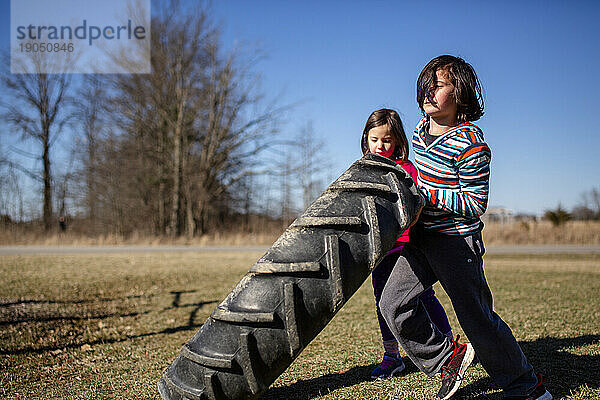 Zwei kleine Kinder arbeiten zusammen  um in einem Park einen schweren Reifen zu heben