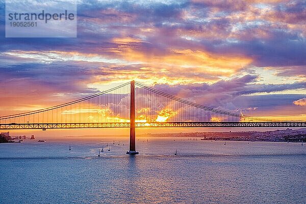 Blick auf die Brücke 25 de Abril  das berühmte touristische Wahrzeichen Lissabons  das Lisboa und Almada auf der Halbinsel Setubal verbindet  über den Fluss Tejo mit Touristenbooten bei Sonnenuntergang. Lissabon  Portugal  Europa