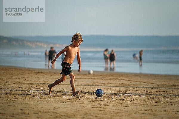 Junge hat Spaß beim Laufen mit Ball am Strand des Atlantischen Ozeans. Fonta da Telha Strand  Costa da Caparica  Portugal  Europa