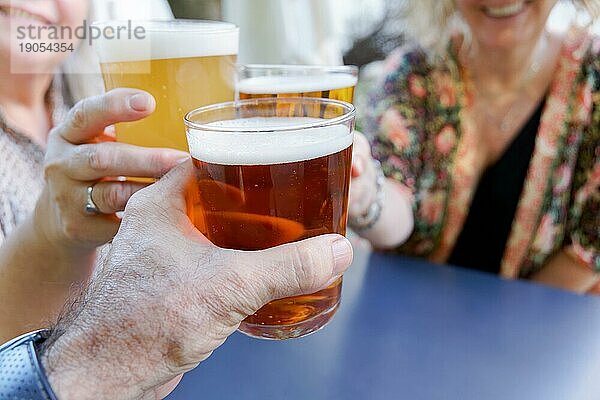 Zwei unerkennbare Frauen und ein Mann stoßen lächelnd mit Biergläsern an