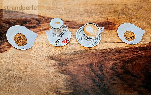 Draufsicht auf heißen Cappuccino mit Keksen auf hölzernem Hintergrund. Hohe Winkelansicht von Cappuccinos mit Keksen auf Holztisch
