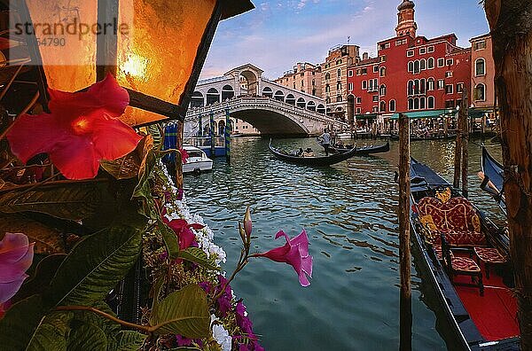 Die berühmte Rialtobrücke oder Ponte di Rialto über den Canal Grande  Venedig  Italien. Ikonisches Reiseziel der UNESCO Welterbestadt. Vorbeifahrende oder vertäute Gondeln  beleuchtete Laterne. Bunte Renaissancefassaden von Gebäuden am Wasser. Selektiver Fokus