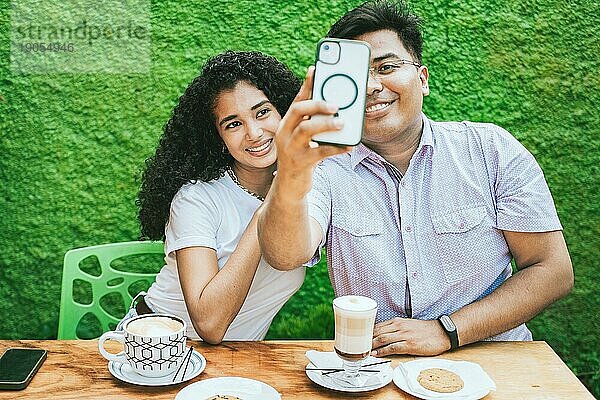Zwei lateinamerikanische Freunde genießen einen Kaffee und machen ein Selfie. Glückliche lateinamerikanische Freunde  die einen Kaffee trinken und ein Selfie machen