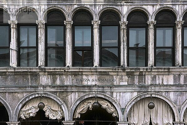 Frontalaufnahme der Fassade des Gebäudes der Procurate Vecchie auf dem Markusplatz  Venedig  Italien. Gleichmäßige Reihen von Arkaden und Fenstern im Stil der Renaissance  gealterter Stein  Inschrift auf Italienisch. Übersetzung  Markusplatz