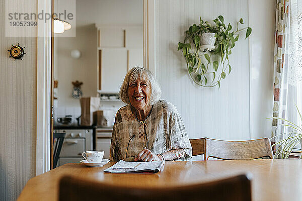Porträt einer glücklichen älteren Frau  die zu Hause am Esstisch sitzt