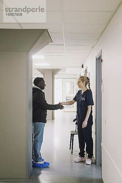 Weibliche Krankenschwester beim Händeschütteln mit einem männlichen Patienten auf dem Krankenhausflur