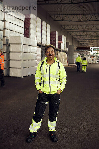 Porträt einer lächelnden Arbeiterin in reflektierender Kleidung  die in einer Fabrik steht