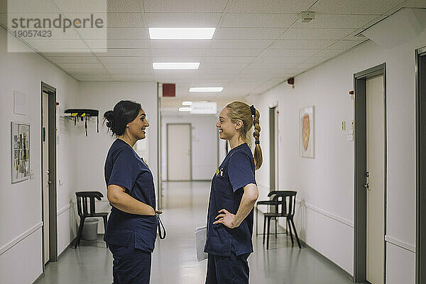 Seitenansicht eines lächelnden weiblichen medizinischen Personals  das in einem Gesundheitszentrum miteinander spricht