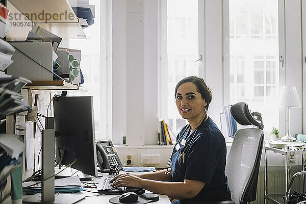 Seitenansicht Porträt der Krankenschwester sitzt am Schreibtisch mit Computer in der Klinik