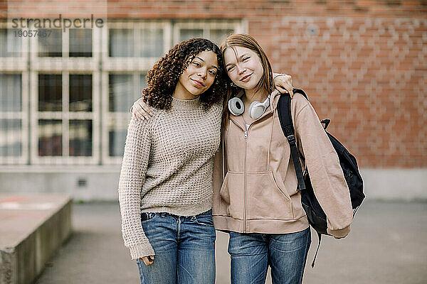 Porträt von lächelnden Studentinnen  die auf dem Campus einer High School stehen und sich umarmen