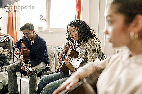 Lächelndes Teenager-Mädchen  das mit Freunden im Musikunterricht an der High School Gitarre übt