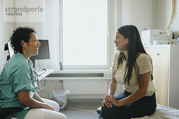 Lächelnder reifer Arzt und weiblicher Patient diskutieren in der Klinik sitzend