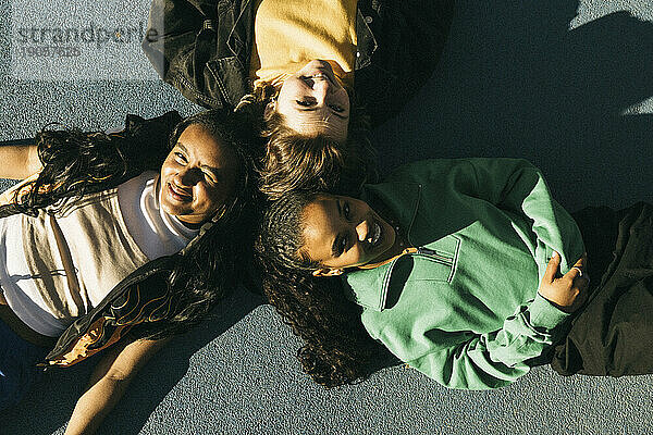 Blick von oben auf lächelnde  am Boden liegende Freundinnen an einem sonnigen Tag