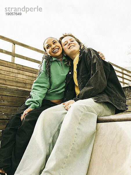 Lächelnde junge Frau  die ihre Freundin umarmt  während sie auf einer Treppe sitzt