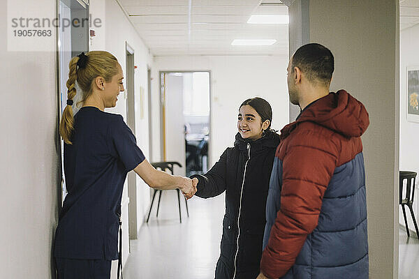 Lächelndes Mädchen schüttelt Hände mit einer Krankenschwester im Krankenhausflur