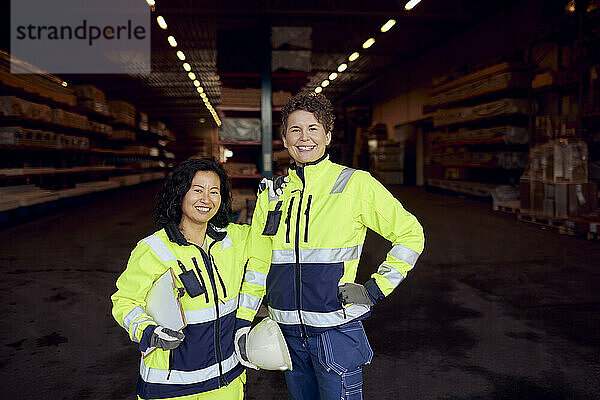Porträt einer lächelnden multirassischen Mitarbeiterin in Arbeitskleidung  die in einer Fabrik steht