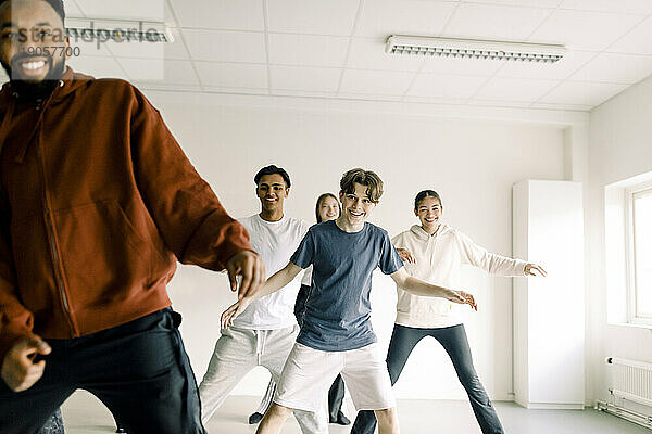 Lächelnder Junge  der mit Freunden und einem Lehrer im Studio der High School tanzen lernt