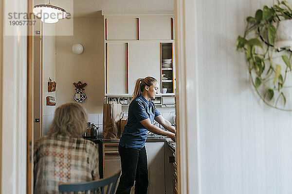 Seitenansicht einer Pflegehelferin bei der Arbeit in der Küche eines Hauses