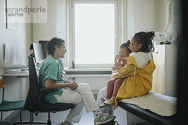 Glückliche Frau  die ihre Tochter trägt  im Gespräch mit einer Kinderärztin im Krankenhaus